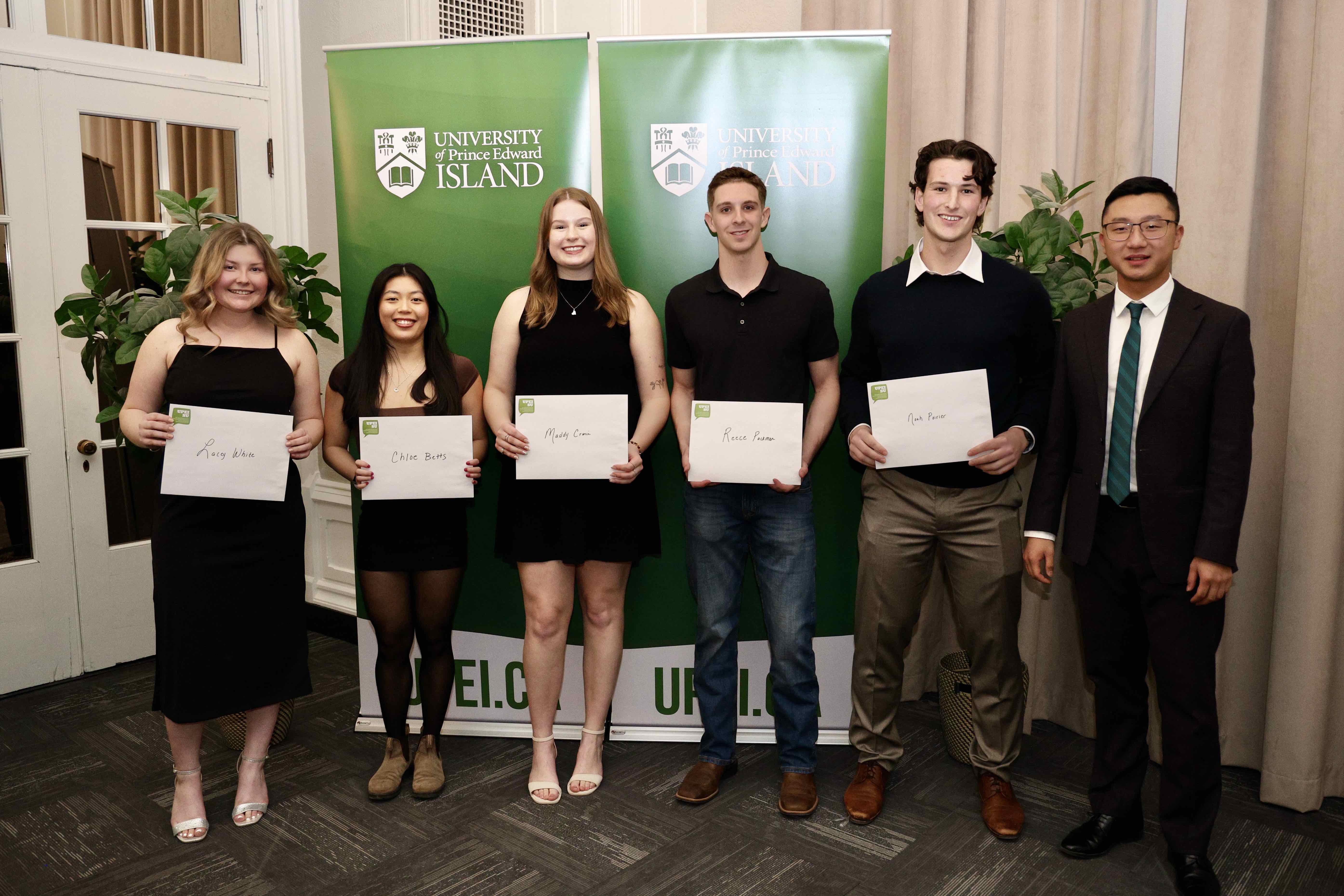 Six smiling people standing together, some holding white envelopes
